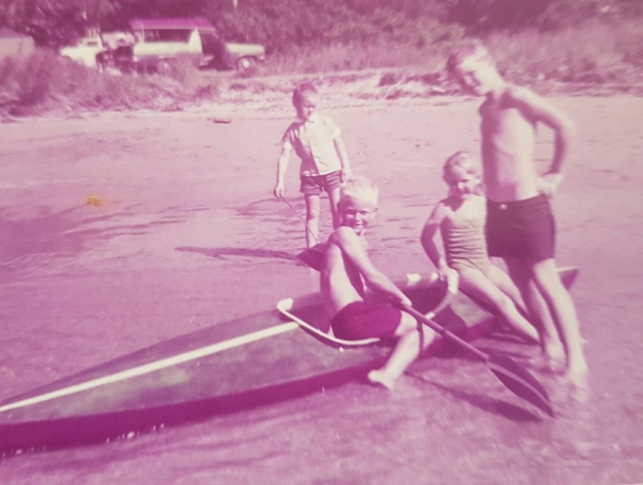 Un tirage couleur passé montrant des enfants sur un surfski au bord de l'eau.